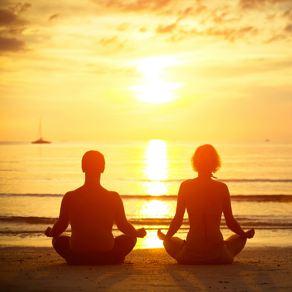 Young couple in a lotus position meditating on the beach at suns