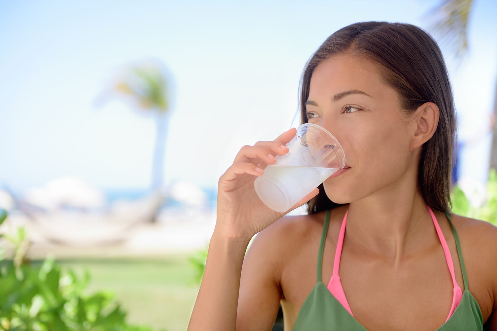 Young woman drinking fresh water or lime juice at beach. Female