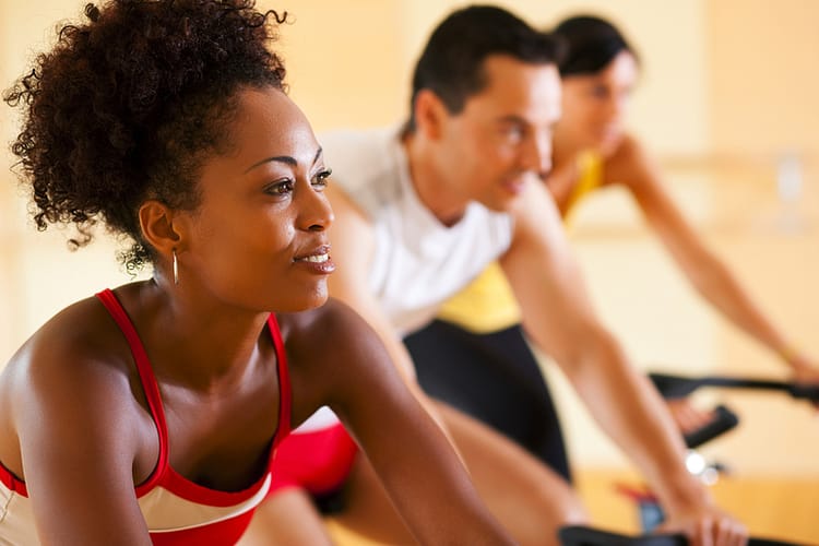 three people in the gym exercising on cycles